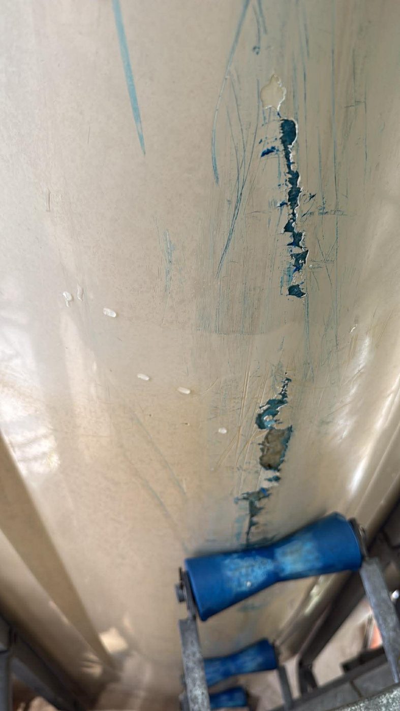 Boat keel with gelcoat chipped and marked by blue trailer rollers before repair, Brisbane