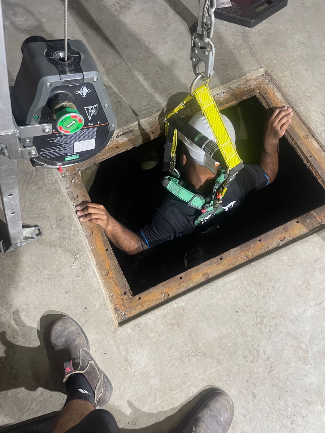 Technician entering a water tank through the floor hatch on a rescue winch line, Brisbane