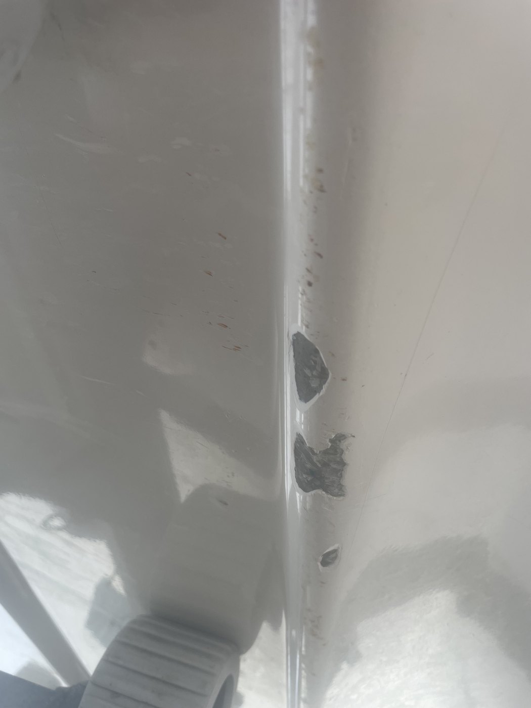Gelcoat chips along a boat hull strake exposing the dark laminate underneath, Brisbane